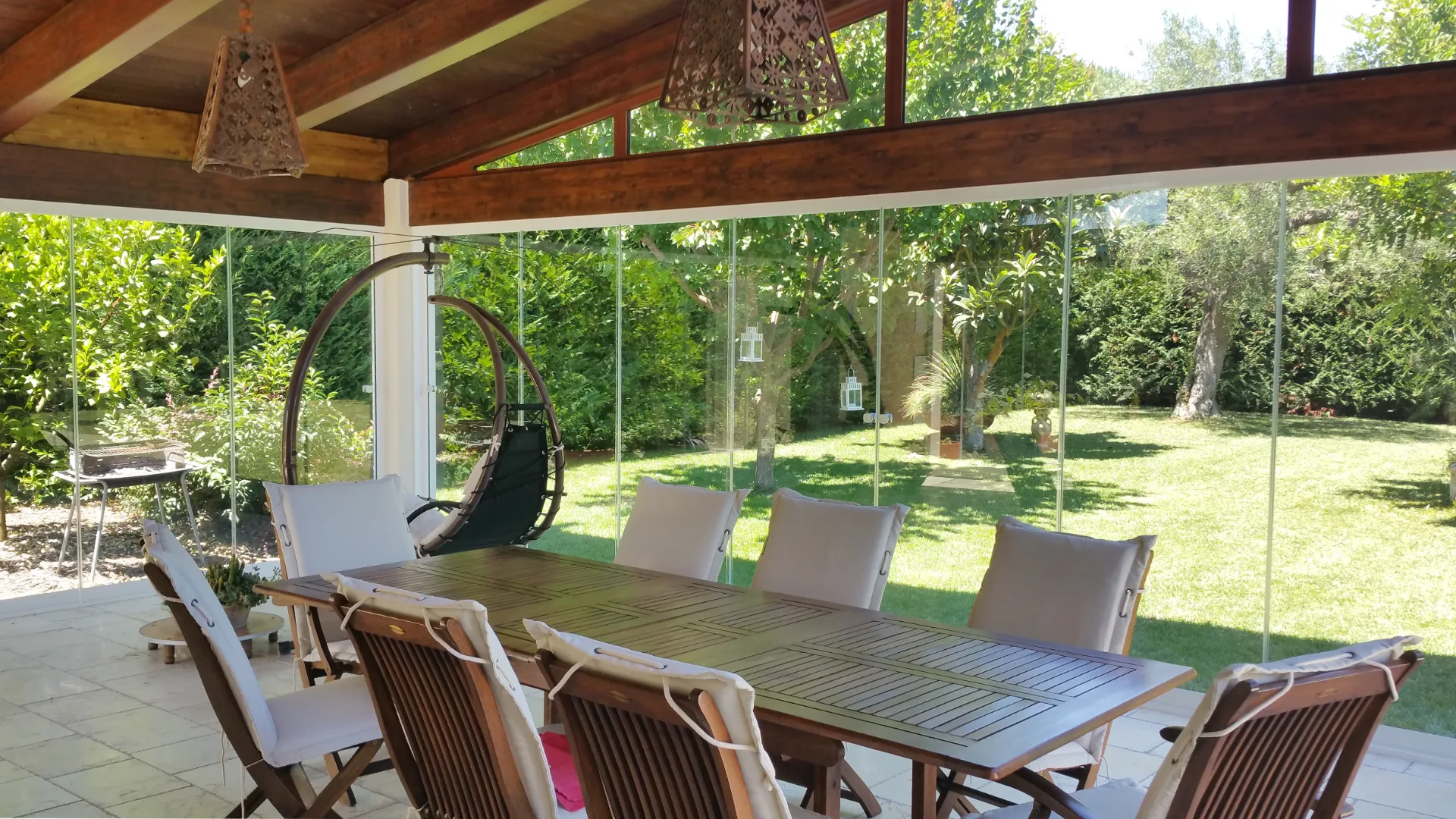 Comedor exterior abierto al jardín mediante paneles de cristal